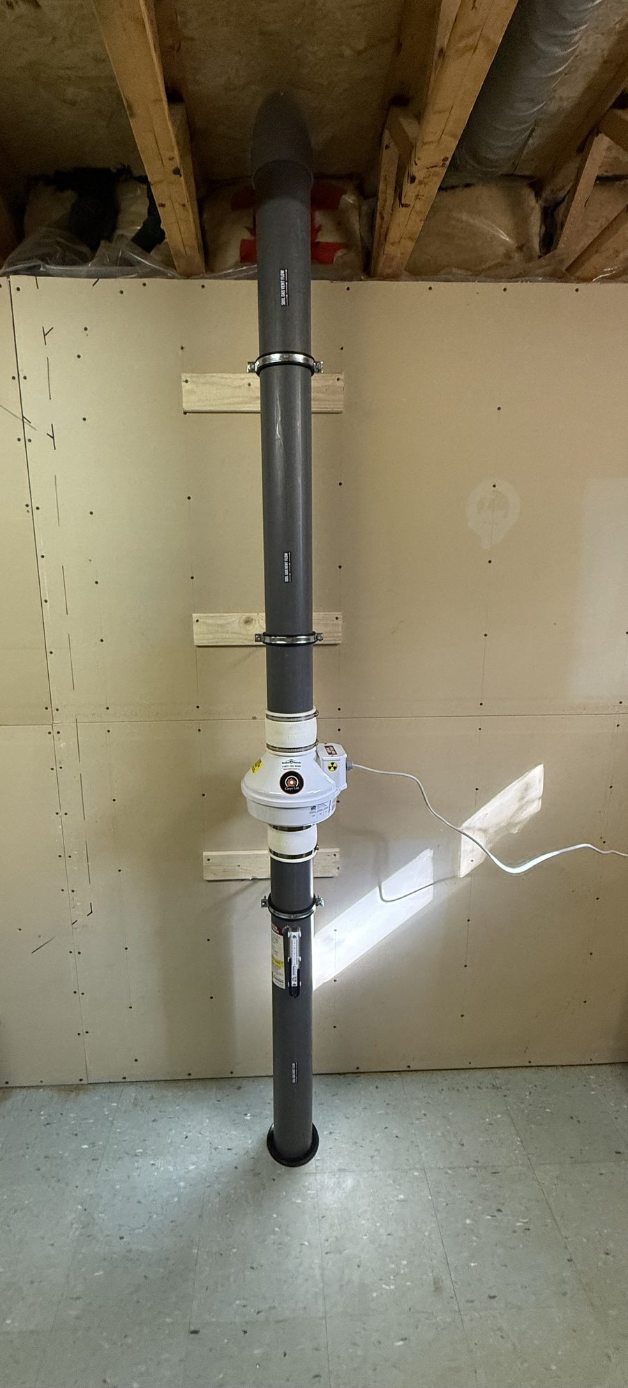 Radon fan and pipe running floor to ceiling on a basement wall